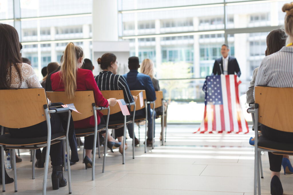 Front view of mixed race businessman speaks at a business seminar in office building with american flag