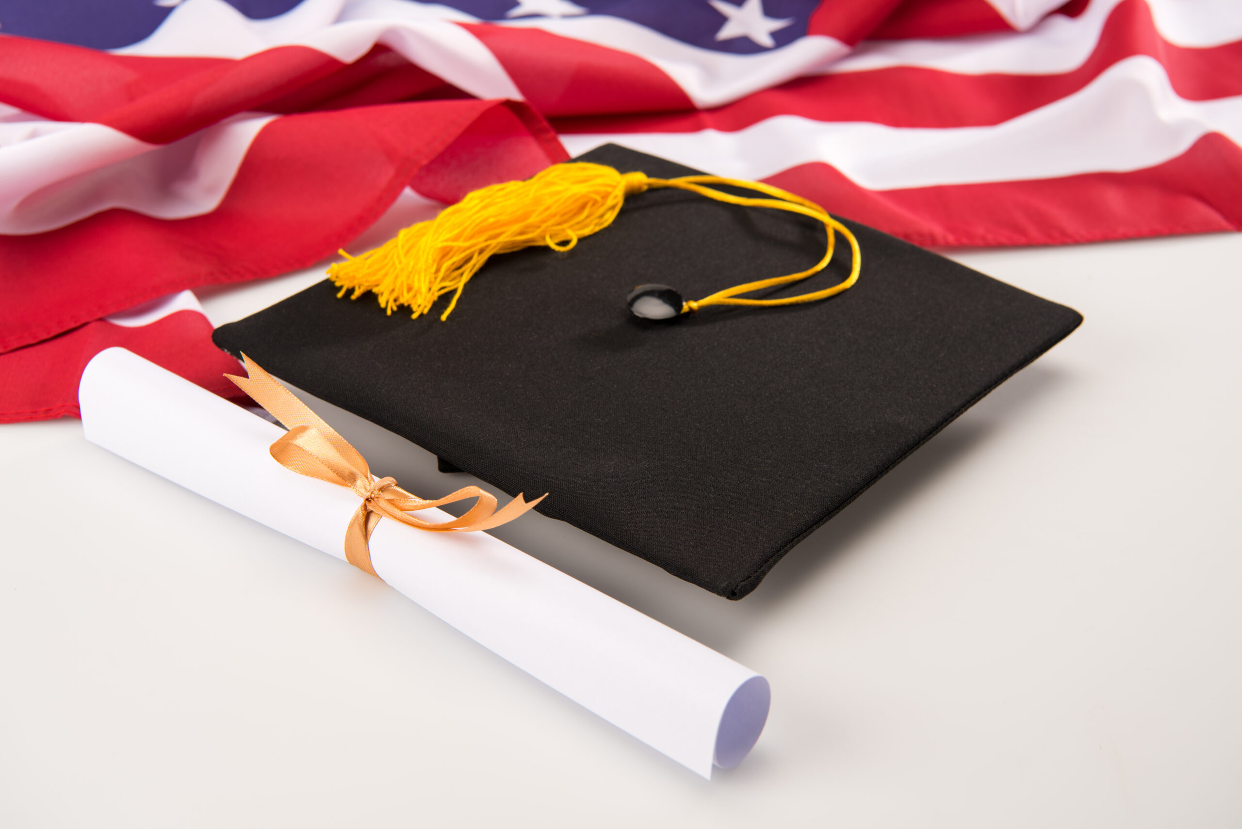 Close up view of graduation mortarboard, diploma and us flag on grey, education concept