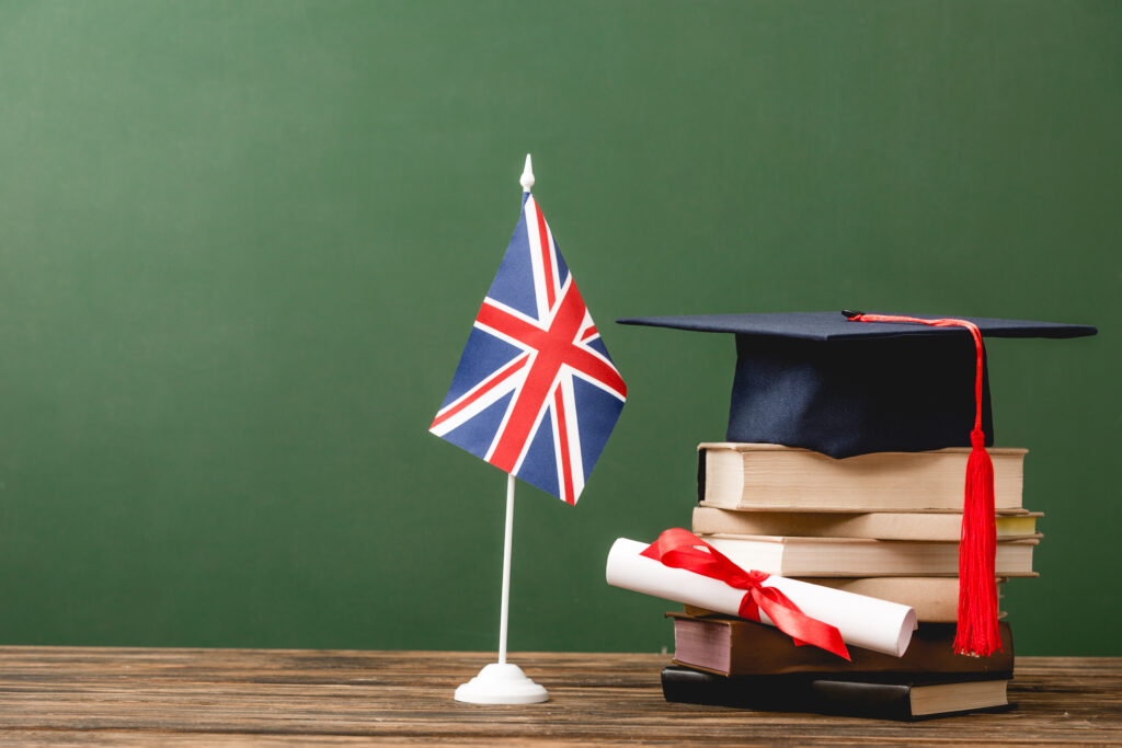 Books, academic cap, diploma and british flag on wooden surface isolated on green
