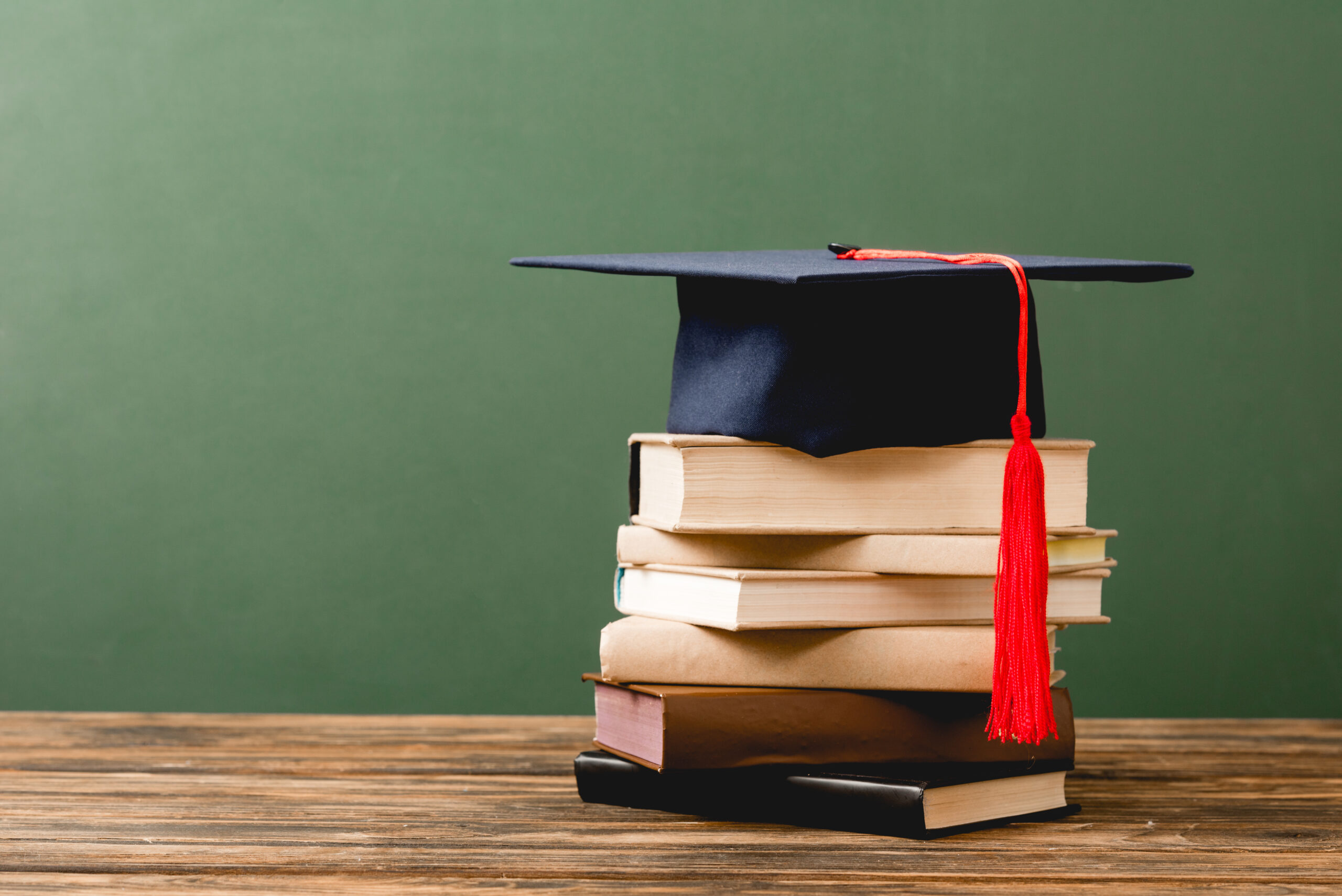 books and academic cap on wooden surface isolated on green