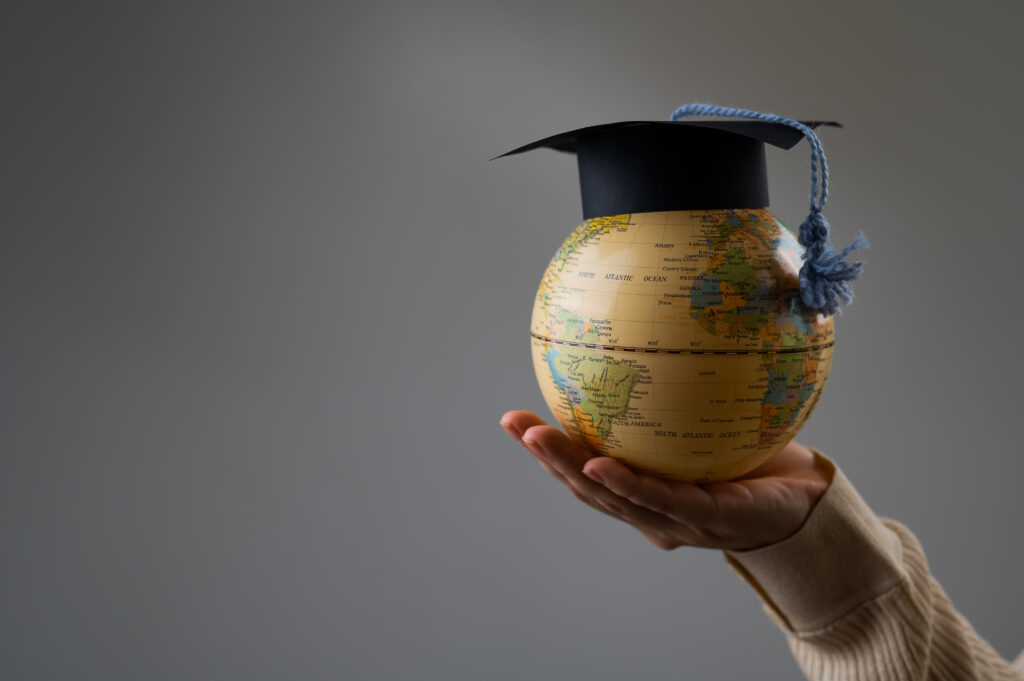 Woman holding a globe wearing a graduation cap.