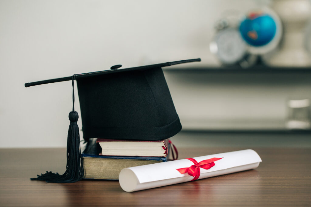 A mortarboard on books and graduation scroll on the desk.educati